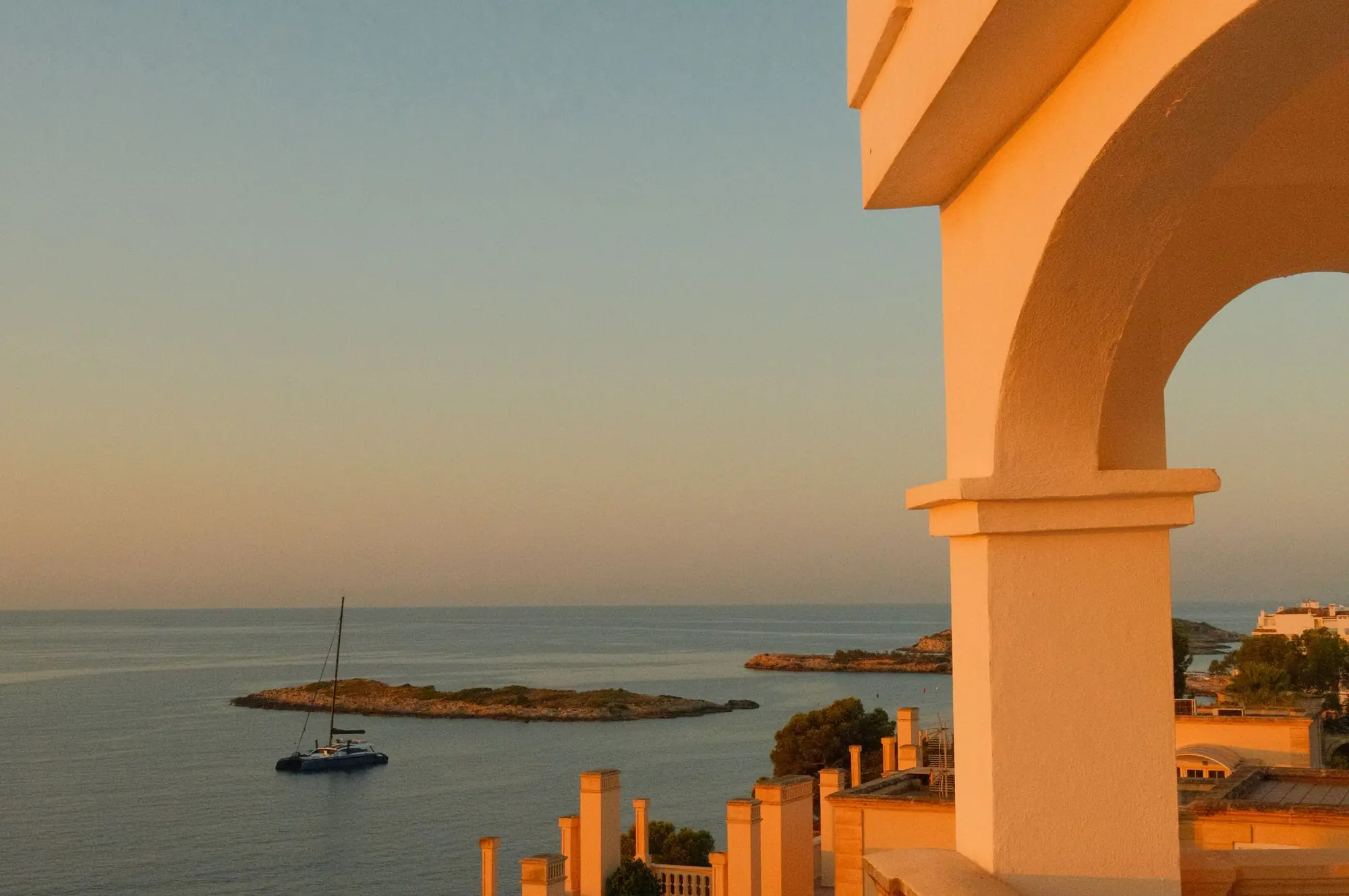 Mediterrane villa boven de zee bij gouden zonsondergang, met een zeilboot op het water, Costa Blanca, Spanje